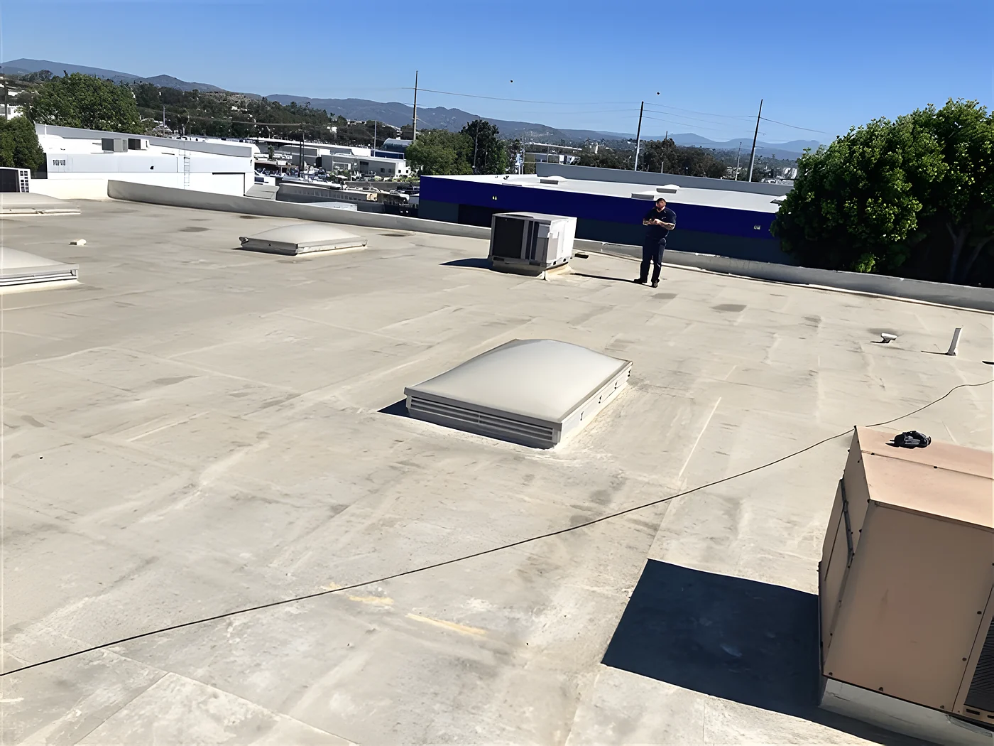 An inspector walking the flat roof of a commercial building, checking the membrane and the rooftop units