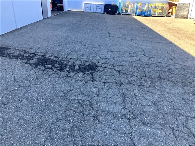 Cracking across the asphalt paving of a commercial parking lot, recorded as a site finding