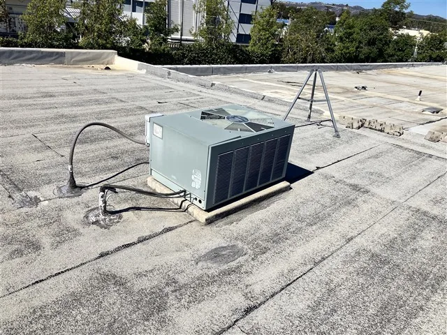 A rooftop HVAC unit and its refrigerant lines on the roof of a commercial building