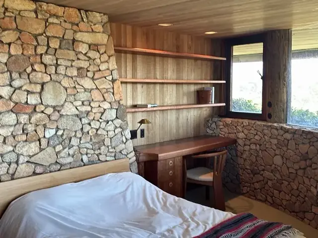 Bedroom interior: stone wall, timber ceiling, built-in shelving and window