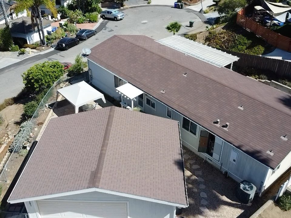 Aerial drone shot looking down at a residential property showing two asphalt shingle roof sections with the surrounding street and neighboring homes visible
