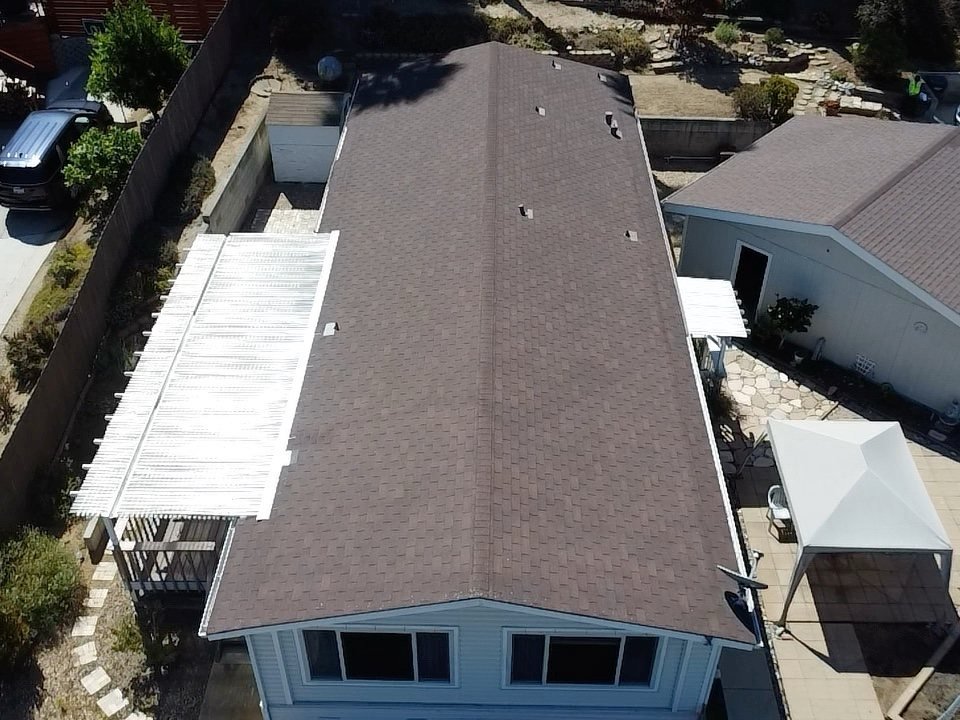 Top-down aerial drone photograph of a residential home showing the full asphalt shingle roof with ridge vents and pergola structures visible in the yard below