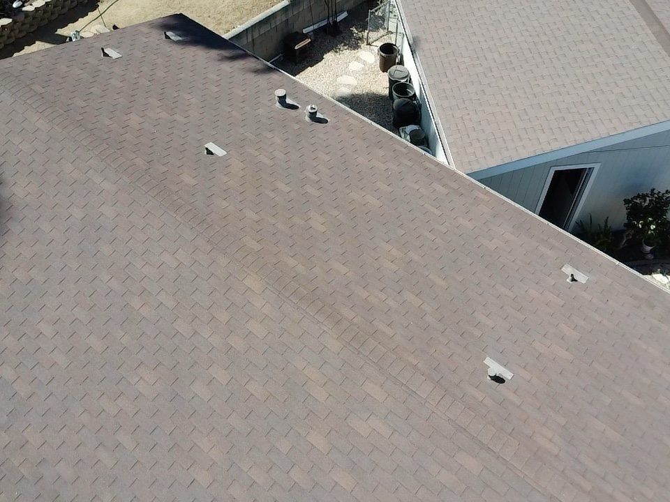 Aerial drone shot looking down on brown asphalt shingle roof with multiple vent pipes and rooftop penetrations