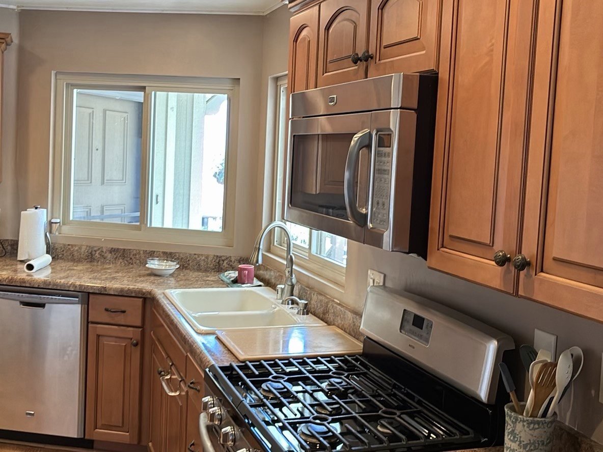 Kitchen interior with warm wood cabinetry, gas range, stainless over-range microwave, double sink, and natural window light