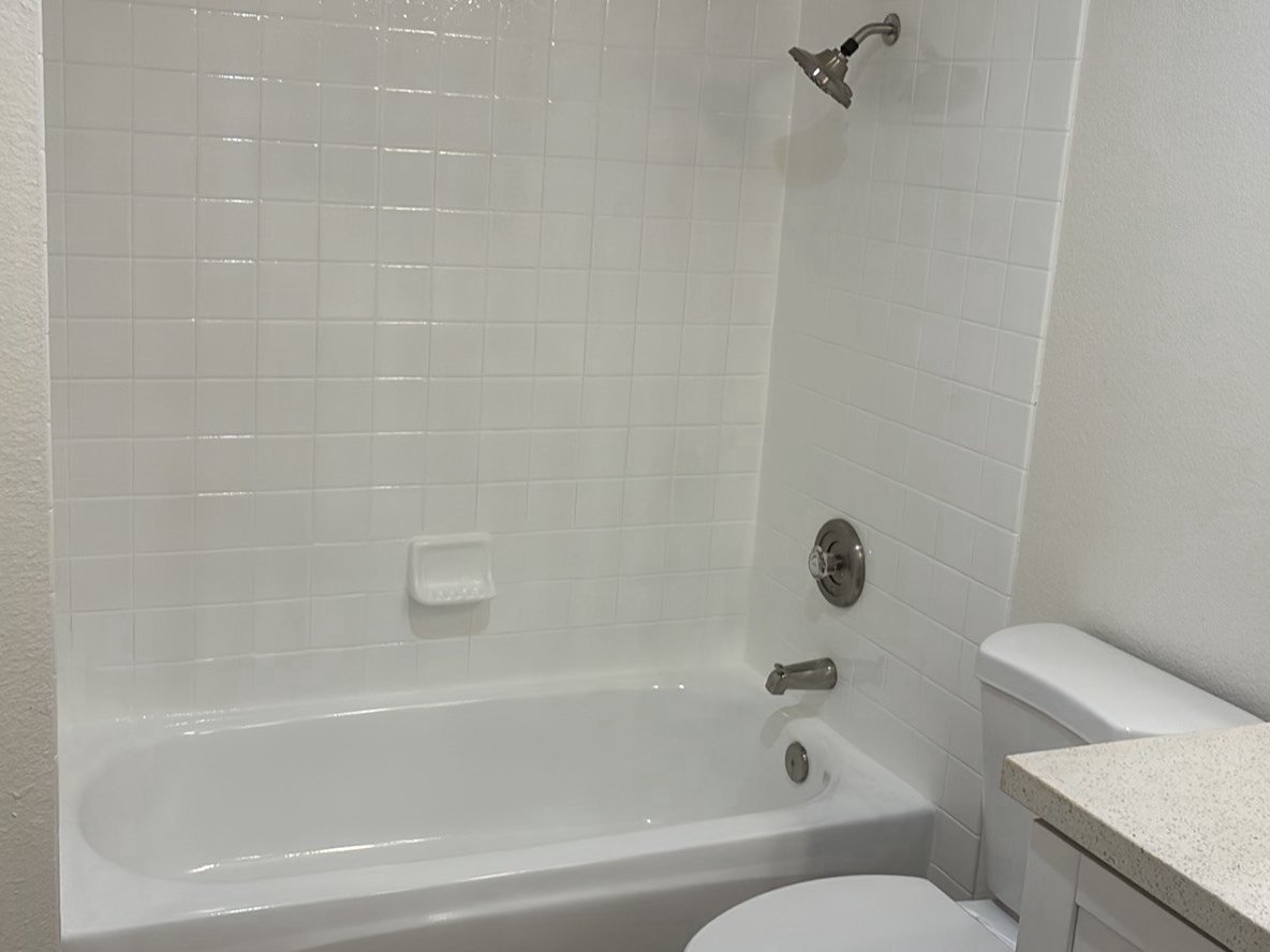 Brand-new white tile tub and shower surround with brushed nickel fixtures in a new construction bathroom