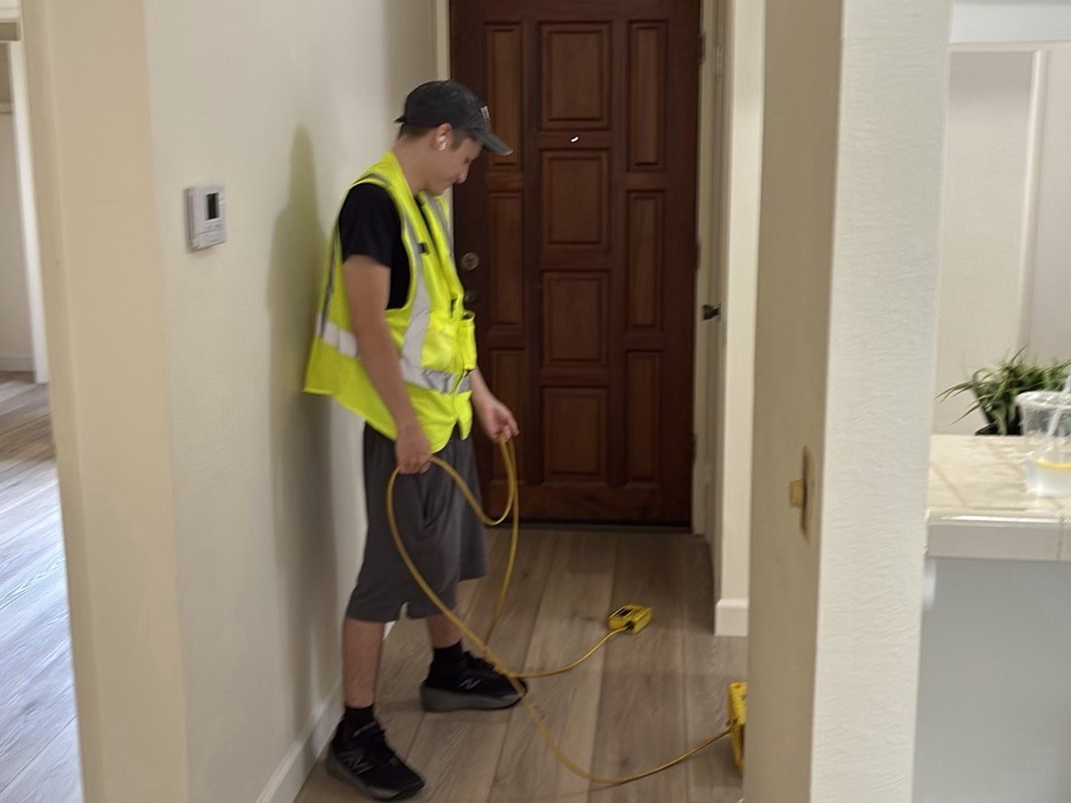 Home inspector in yellow safety vest operating a yellow ZipLevel electronic altimeter device on the floor of a residential property during a concrete slab elevation survey