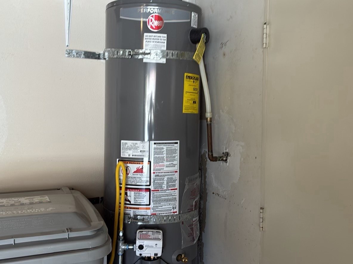 New Rheem gas water heater with yellow EnergyGuide label and earthquake straps in a residential garage