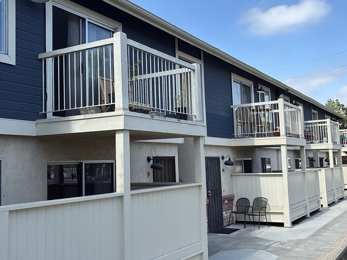 Two-story townhouse-style condominium complex showing multiple second-floor private balconies with white metal railings and blue siding, inspected under SB-326