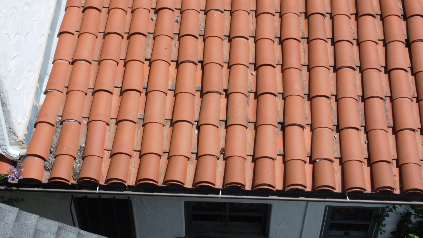 Clay barrel tile roof eave detail with aluminum rain gutter attached to fascia board at roof edge