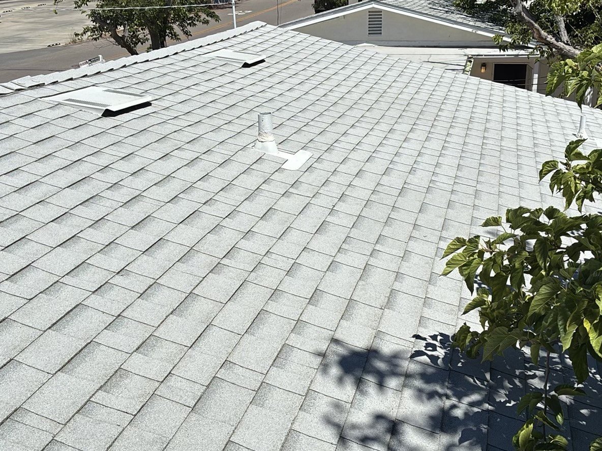 Asphalt shingle roof with skylight and white plumbing vent boot viewed from rooftop during home inspection
