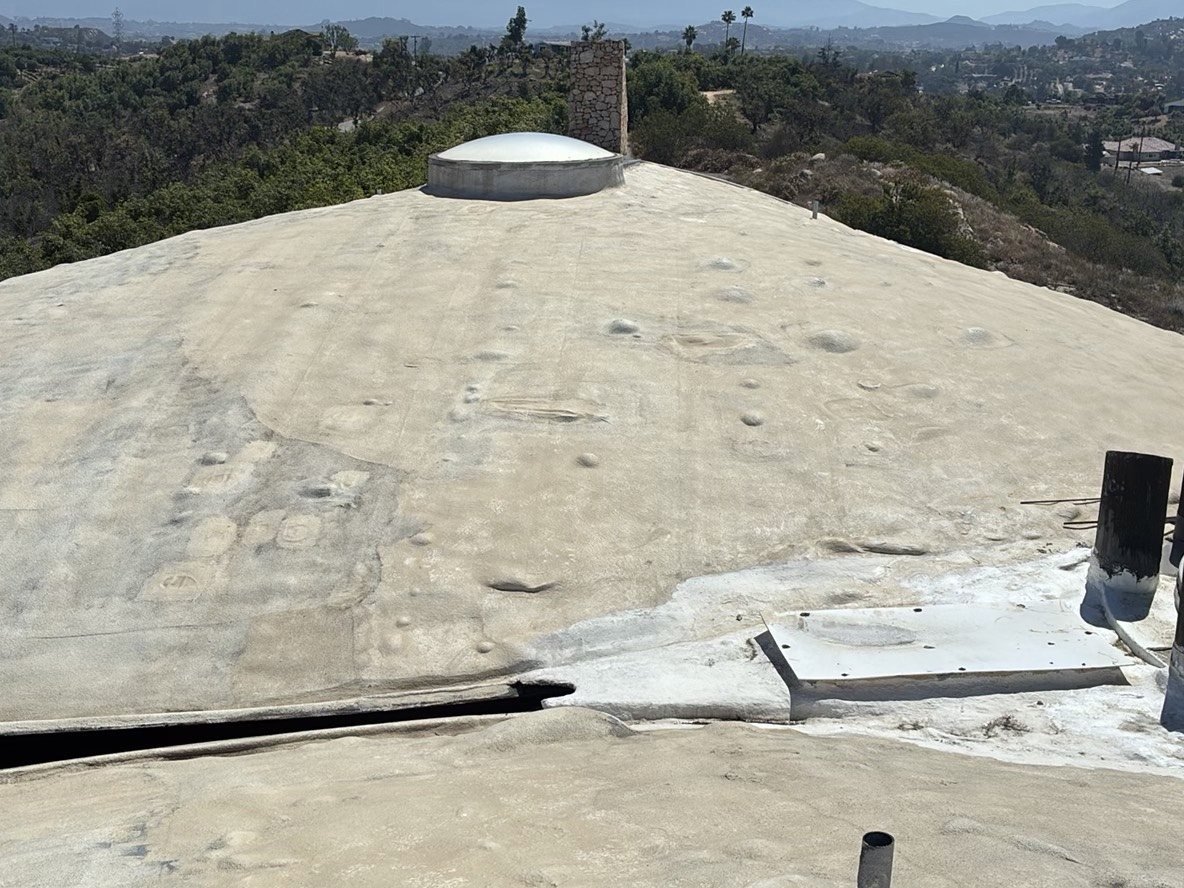 Flat spray-foam elastomeric roof coating with bubble skylight dome and pipe penetrations on hilltop property