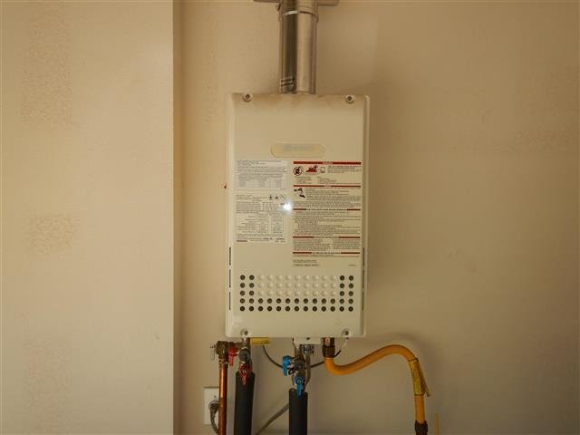 Modern tankless gas water heater mounted on interior wall with flue and supply lines