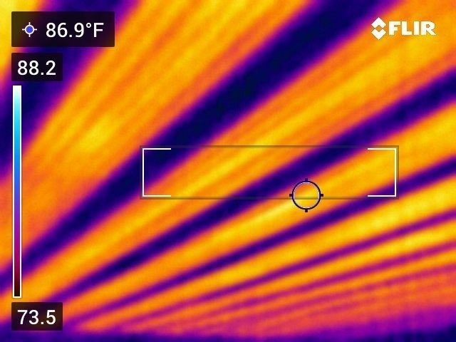 FLIR thermal scan of a ceiling with embedded radiant heat cables showing evenly spaced warm orange and yellow stripes across the entire surface