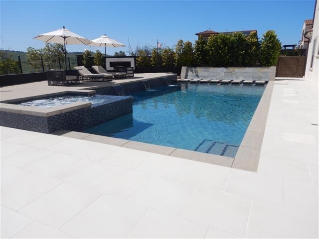 Modern rectangular swimming pool with an elevated square spa, sheet-flow waterfall wall, lounge chairs, and pergola on a property