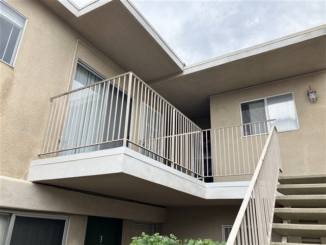 Exterior view of second-floor balcony with cream steel guardrails and concrete staircase on stucco apartment building