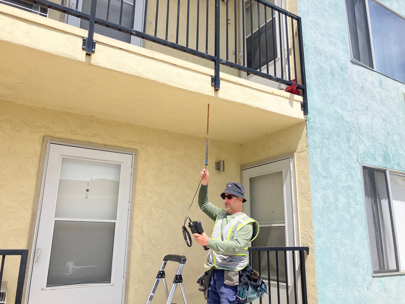 Inspector reaching a pole-mounted tool to a balcony soffit