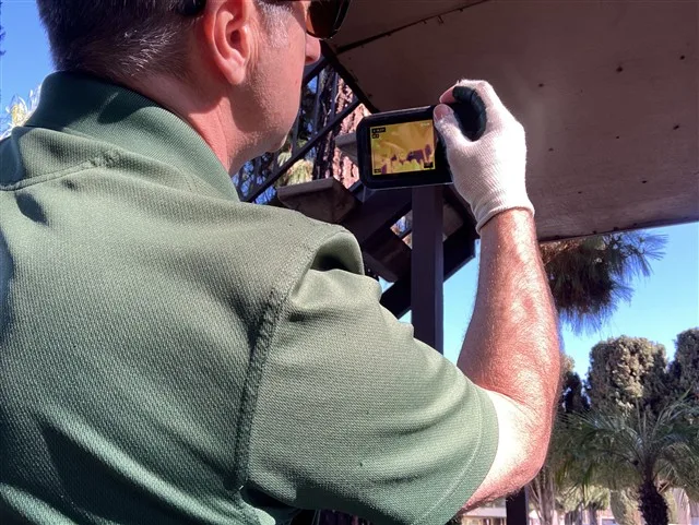 Home inspector using an infrared thermal imaging camera to scan a balcony underside for hidden moisture during a San Diego inspection.