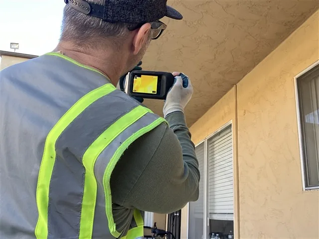 Home inspector aiming an infrared thermal camera at an exterior wall and soffit during a San Diego inspection.